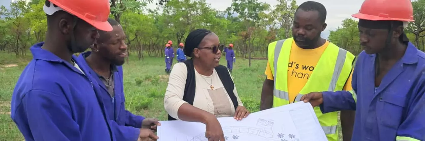 Sister Loice Kashangura discussing blueprints with construction workers.